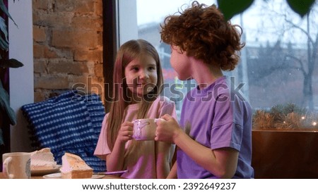 Cute happy children holding together one cup of hot sweet drink. Stock footage. Boy and girl, sister and brother at a cafe.