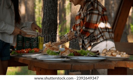 Mother and adult daughter serving outdoors wooden table. Stock footage. Having bbq with family in summer forest.