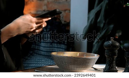 Side view of woman hands making photo of a dish in plate on mobile phone while sitting in comfortable restaurant. Stock footage. Female taking pictures with cell phone camera of delicious dish.