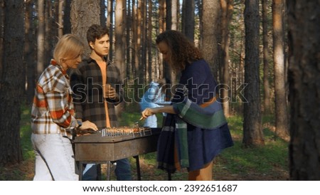 Friends cook grilled meat in forest in summer. Stock footage. Beautiful friends are relaxing in nature with barbecue in forest. Relaxing with friends in nature with barbecue on sunny summer day