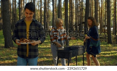 Friends cook grilled meat in forest in summer. Stock footage. Beautiful friends are relaxing in nature with barbecue in forest. Relaxing with friends in nature with barbecue on sunny summer day