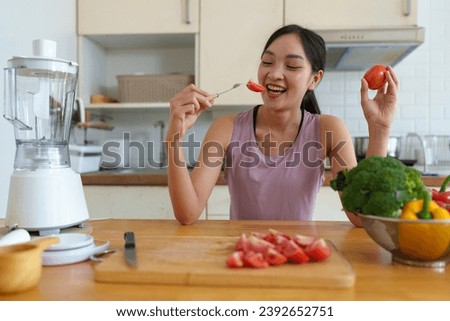 Beautiful young woman in exercise clothes is cutting tomatoes to eat for good skin and health. Refreshing after a happy workout inside the house. Food concept. Vegetables, useful fruits. Lifestyle.