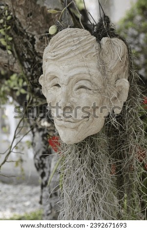 Vertical Photo of a Potted White Human Head Sculpture with white roots and plants hanged in a garden setting. Royalty-Free Stock Photo #2392671693
