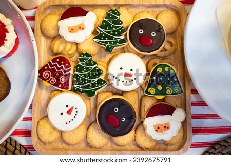 Christmas cookie homemade with sugar icing painted cartoon character of Santa Claus, Pine Tree, Snowman, Jingle Bells and Gingerbread Man on wooden tray for dinner party