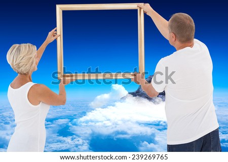 Mature couple hanging up picture frame against mountain peak through the clouds
