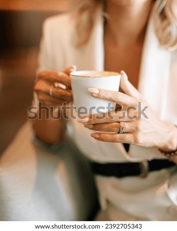 Woman with a cup of coffee sits in a chair, leaning on the handrail. Cropped. Faceless Royalty-Free Stock Photo #2392705343