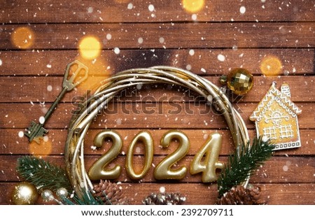 House key with keychain cottage on festive brown wooden background with stars, lights of garlands. New Year 2024 wooden letters, greeting card. Purchase, construction, relocation, mortgage, insurance