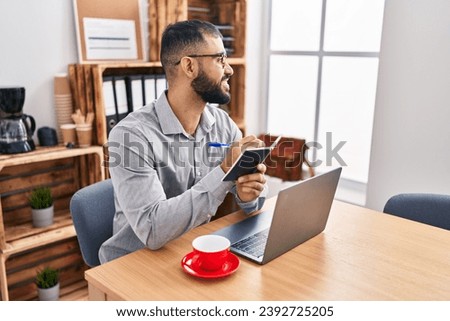 Young hispanic man business worker using laptop writing on notebook at office