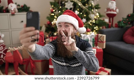 Young redhead man make selfie by smartphone sitting on floor by christmas tree at home