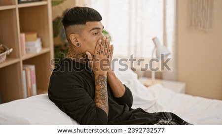 Stressed young latin man sitting on bed, wrestling with anxiety as morning breaks in his bedroom, mirroring the emotional struggle within his tattooed portrait, manifesting as a throbbing headache