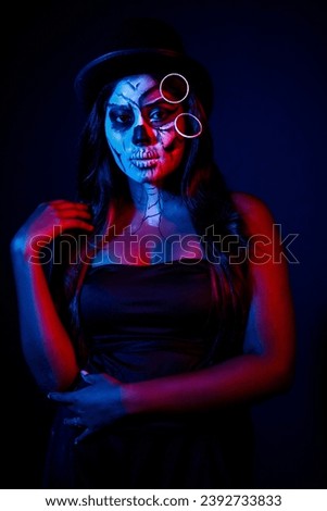A women with Halloween Makeup in blue red light giving out a horror look wearing black gown in black background