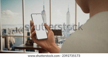 CU 30s Caucasian male holding a generic smart phone in vertical orientation, bright open space office in background, white screen smartphone banking, work application app mockup