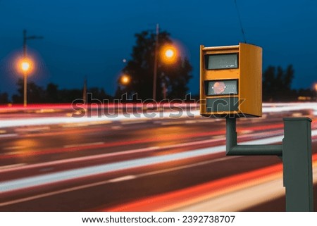 A radar-equipped speed camera monitors the traffic on a road, flashing a yellow light when it catches a car exceeding the speed limit, and using technology to identify the vehicle and enforce the law. Royalty-Free Stock Photo #2392738707