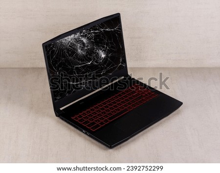 black gaming laptop with broken screen on a gray background side view