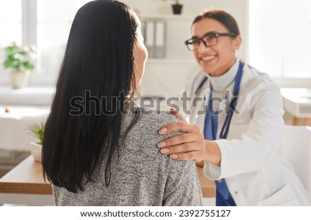 Portrait of smiling friendly doctor support female patient putting hand on her shoulder. Physician wearing stethoscope giving consultation a woman sitting back during medical examination in clinic. Royalty-Free Stock Photo #2392755127
