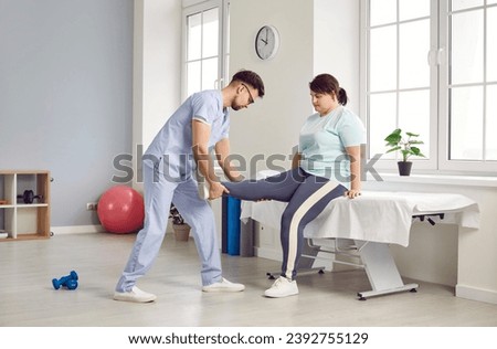 Physiotherapist doing leg massage. Woman undergoing physiotherapy treatment. Man in medical uniform massaging leg muscles of young fat woman in sportswear sitting on massage table at clinic Royalty-Free Stock Photo #2392755129