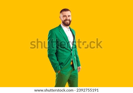 Studio shot of happy young man in green suit. Portrait of handsome male model wearing stylish green suit posing with his hand in pocket isolated on yellow color background. Male fashion concept