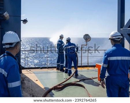 Seamen during fire emergency training drill, on board a merchant cargo ship, wearing fire fighting equipment and helmets. Rigged fire hose for jet spray, with emergency fire pump. Royalty-Free Stock Photo #2392764265