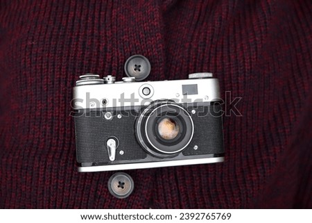 Retro film photo camera  on red knitted sweater background. Old retro camera on vintage abstract background. Close up.