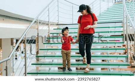 Mother with little son descending  on stairs at shopping mall. Little caucasian boy in casual sharing impressions after cinema with mom. Family at shopping, sales, discount.