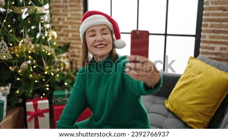 Mature hispanic woman with grey hair taking a selfie picture sitting on the sofa at home