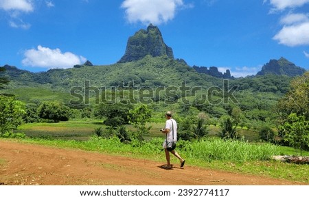 Man walking on dirt road with the dramatic jagged mountains of Moorea in the background - Moorea, French Polynesia Royalty-Free Stock Photo #2392774117