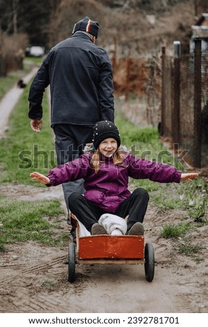 A strong man, father, grandfather rides, carries on a rusty old cart, wagon along the road in the village, countryside, a small smiling, happy girl, a child. Photography, portrait, emotions.