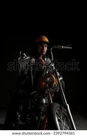 Man rider on a yellow chopper custom motorcycle standing in an authentic style, dark background with dramatic backlight