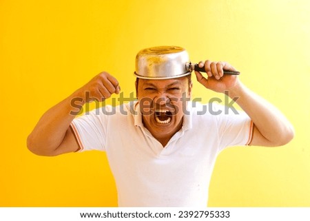Asian man's angry expression while placing a pot on his head