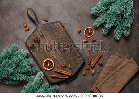 Christmas spices on a wooden cutting board decorated with decorative fir branches, dark brown background. Top view, flat lay, copy space