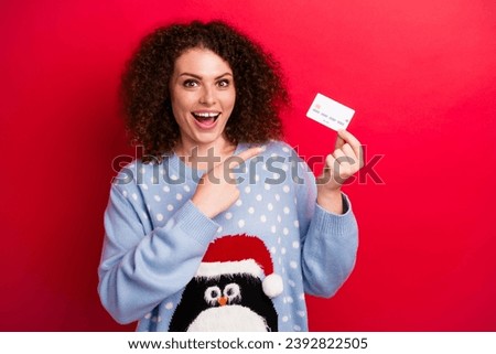 Photo of surprised young curly lady point finger payment card recommend christmas shopping with cashback isolated on red color background