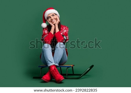 Full size photo of young cute girl touch cheeks dreaming looking empty space ride sledge santa claus isolated on green color background