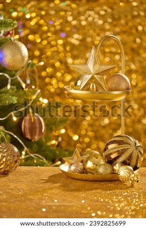 Two-tiered jewelry storage tray containing a lot of sparkling baubles and stars decorated with a christmas tree behind. Another word for the Christmas season is Christmastime