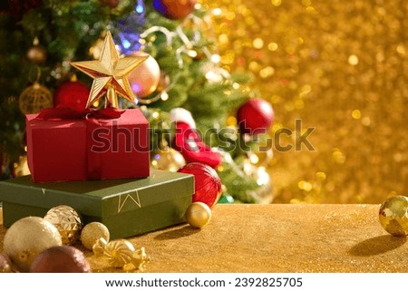 A stack of gift boxes and a star placed on top arranged with colorful baubles. Vacant space for product advertising. Holiday illumination and decoration concept