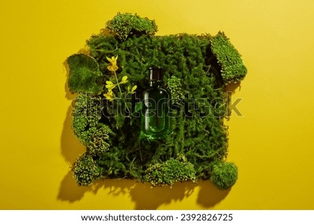 Background for advertising cosmetics with green glass bottle mockup placed on green moss carpet with yellow flower on yellow background. Top view, minimal concept, space for design