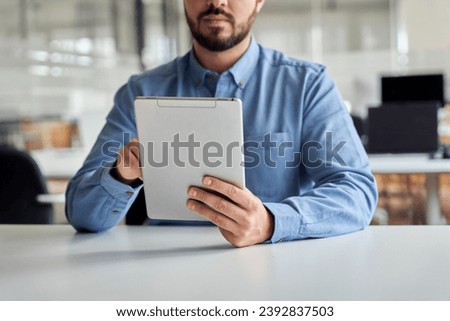 Busy young business man manager using tablet computer, businessman company worker holding tab tech device in hands analyzing financial market data working sitting at office desk. Close up view.