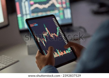 Business man trader broker analyst investor holding tab in hands using digital tablet analyzing stock trade crypto market carts investing finances in stockmarket working in dark night office. Close up Royalty-Free Stock Photo #2392837529