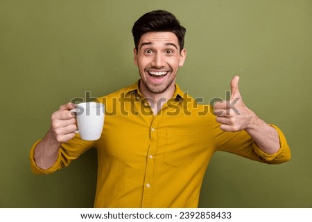 Photo of cheerful nice guy hold aroma coffee mug demonstrate thumb up isolated on khaki color background