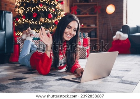 Photo of adorable jolly cheerful girl lying on floor carpet waving hand talking with friends app modern netbook macbook