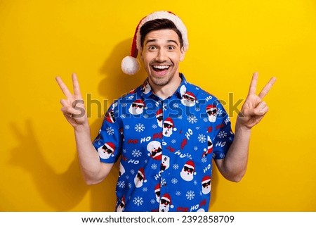 Holly jolly merry xmas party celebrate two hands v sign red hat pom pom blue shirt traditional picture isolated on yellow color background