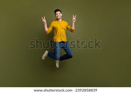 Full length photo of good mood cheerful man wear stylish outfit jump up demonstrate v-sign isolated on khaki color background