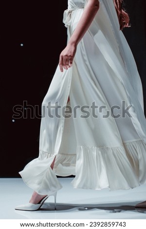 White fashion details of long silky bridal dress. Fashion model walking on black background Royalty-Free Stock Photo #2392859743