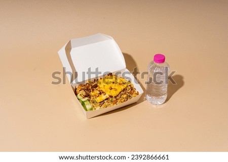 fried rice in a box with fried chicken, cucumber slices and egg. a bottle of mineral water and a beige background