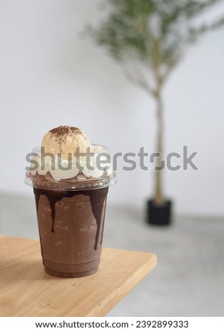 Chocolate Frappe in transparent plastic glass with whipped cream and ice-cream on top, selective focus on glass with blurred background of white wall. For Beverage Concept of any designs.
