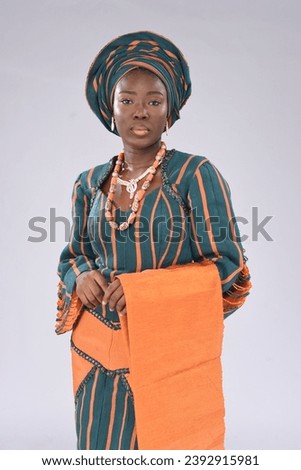 young black yoruba looking gorgeous wearing native attire up tying gele and looking into the camera Royalty-Free Stock Photo #2392915981