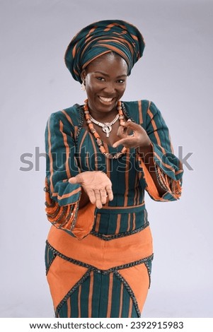 young black yoruba looking gorgeous wearing native attire excited smiling raising up tying gele and surprised feeling happy pointing hand Royalty-Free Stock Photo #2392915983