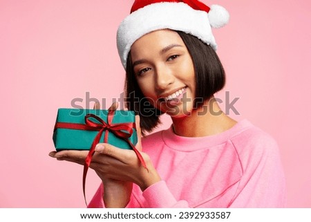 Portrait of cheerful woman wearing Christmas hat, holding green gift box with red ribbon and looking at camera closeup. Conception Celebrations, New Year, Christmas, dental care