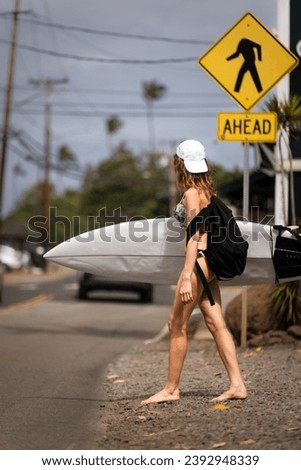 Surfer girl with a surfboard crossing road in hawaii surf town north shore