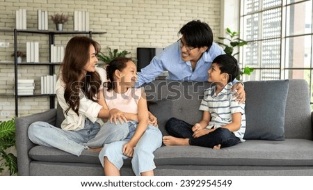 Happy family chatting at home in the living room. A young man stands behind sofa and a young woman sits on the sofa with her son and daughter. Spend happy time together and talk about various topics