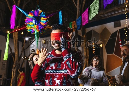 Latin young man breaking a pinata at traditional mexican posada celebration for Christmas eve in Mexico Latin America, hispanic family in holidays